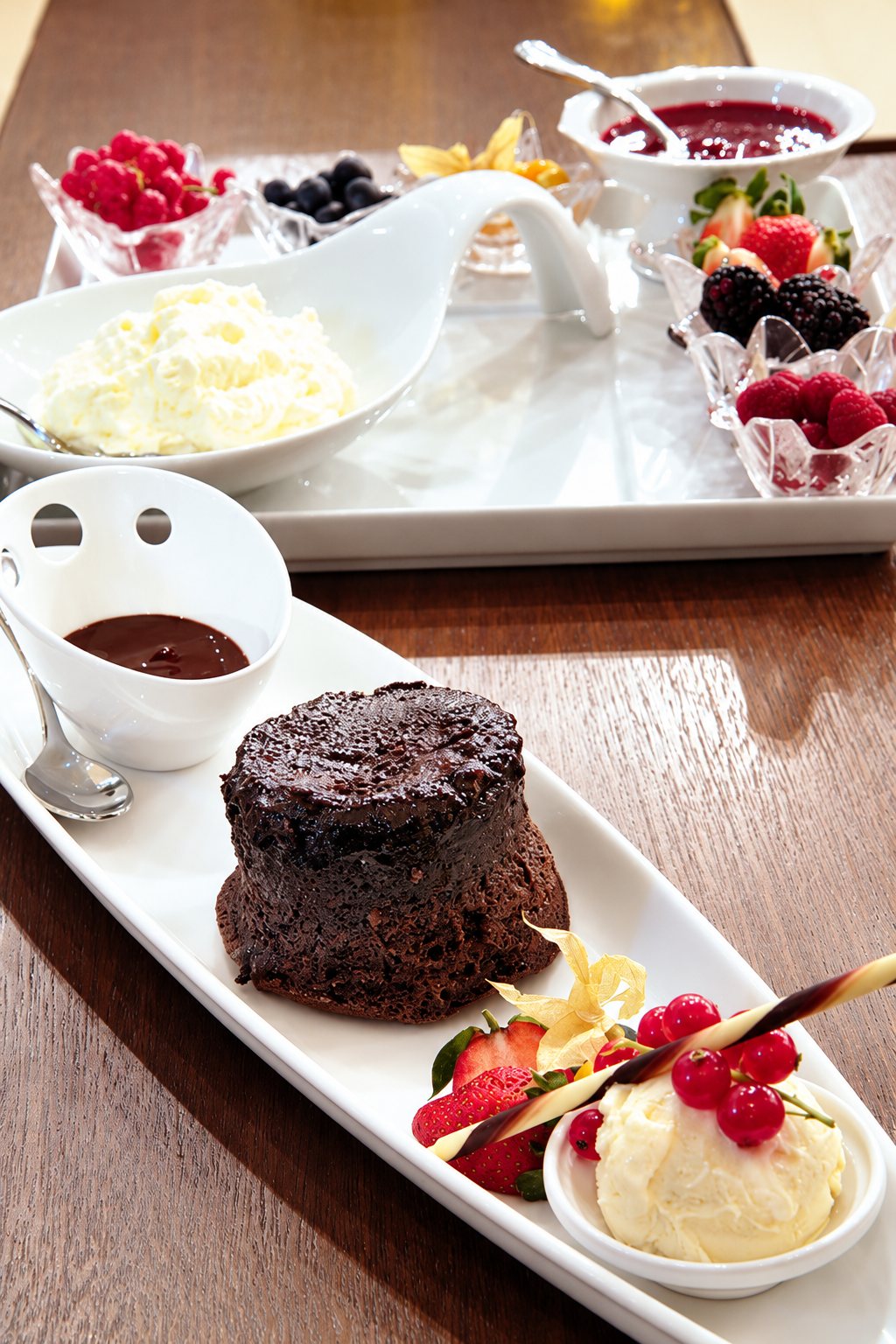 Fondant au chocolat accompagné de glace, de fruits rouges et d’une coupelle de sauce chocolat sur un plateau blanc