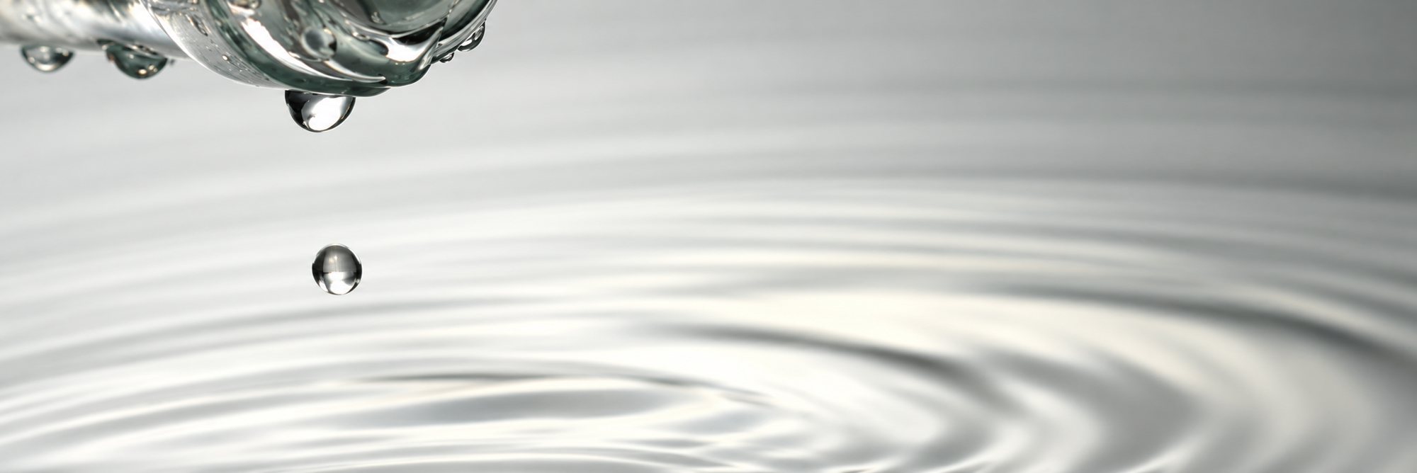Gouttes d’eau tombant d’un robinet en verre et formant des ronds dans l’eau