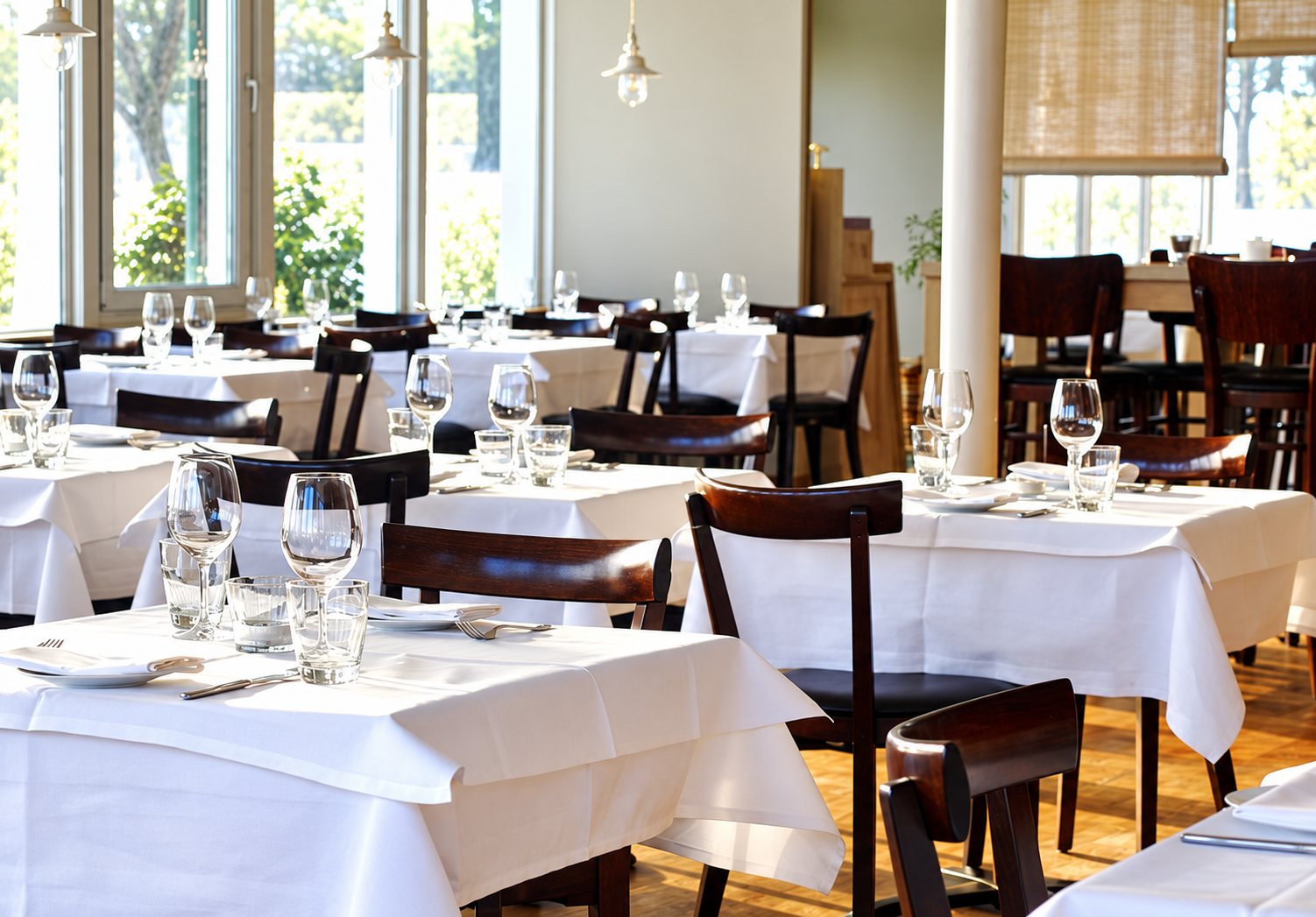 Salle de restaurant aux tables dressées de nappes blanches, chaises en bois sombre et verres