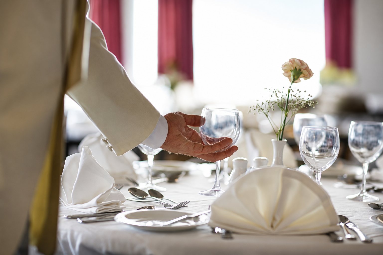 Main d’un serveur tenant un verre au-dessus d’une table dressée avec serviettes pliées et couverts